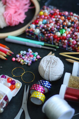 Colorful beads, coloring pencils, glitter, needles, string, hoop, tape and scissors on dark background. Various colorful craft supplies. Selective focus.