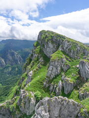 Mountain scenery with a dominant peak covered with green grass and limestone rock formations under a partly cloudy sky