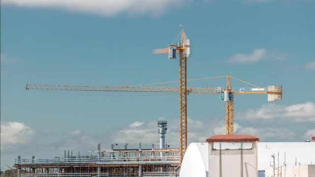 Timelapse of construction site with cranes working on a building complex. Dynamic clouds passing by in close-up view. Industrial progress under changing sky