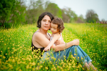 Mother and baby girl daughter playing in a flower field in spring. Concept of mom and daughter bonding and playing together outdoors, shot with vintage lens