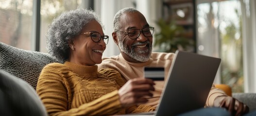 Senior couple enjoying online shopping together, using a credit card and laptop in a cozy home setting.