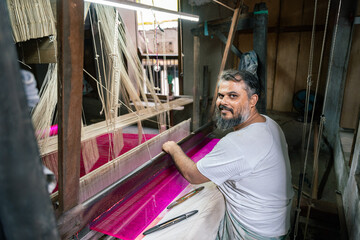 Mature indian artisan working with traditional loom in workshop