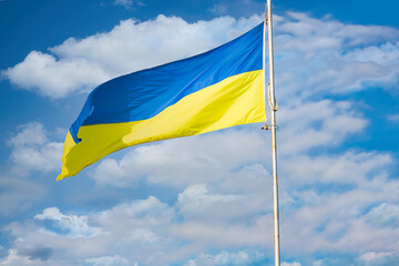 Ukrainian flag waving against a backdrop of white clouds and a clear blue sky