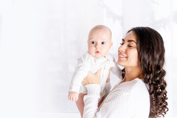 happy mother holding baby daughter at home by the window, mother's day, happy family concept, space...