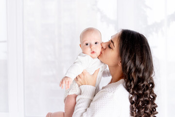 mom and baby, beautiful mother kissing newborn baby holding in his arms a home, the concept of happy loving family, lifestyle