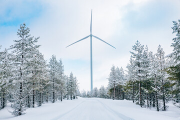 Wind turbines in winter landscape with snow covered trees and snow road in Finland, Europe. Alternative energy in winter.