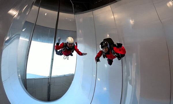 Two individuals engaging in indoor skydiving in a vertical wind tunnel.