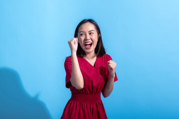 An excited Asian woman in a red dress raises both fists in the air while cheering enthusiastically....