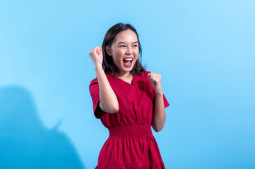 An excited Asian woman in a red dress raises both fists in the air while cheering enthusiastically....