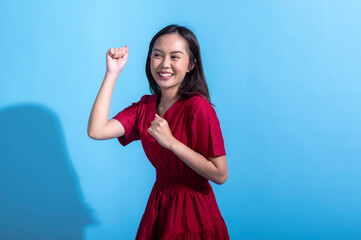 An excited Asian woman in a red dress raises both fists in the air while cheering enthusiastically....