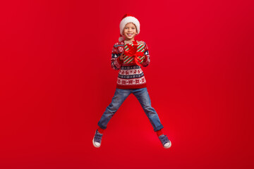 Full body photo of cute little boy jump hold present celebrate christmas wear knitwear sweater isolated on red color background
