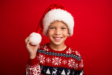 Photo portrait of charming small boy touch hold pompom celebrate christmas dressed knitted sweater isolated on red color background