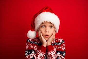 Photo portrait of cute little boy shocked reaction touch cheeks celebrate christmas wear knitwear sweater isolated on red color background