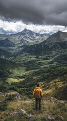 Obraz premium A hiker stands on a mountain peak, overlooking a vast valley surrounded by majestic peaks under a moody sky.