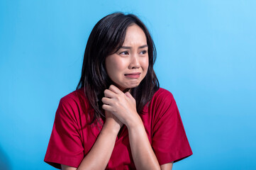 Asian woman in a red dress is standing against a light blue background with a sad and disappointed...