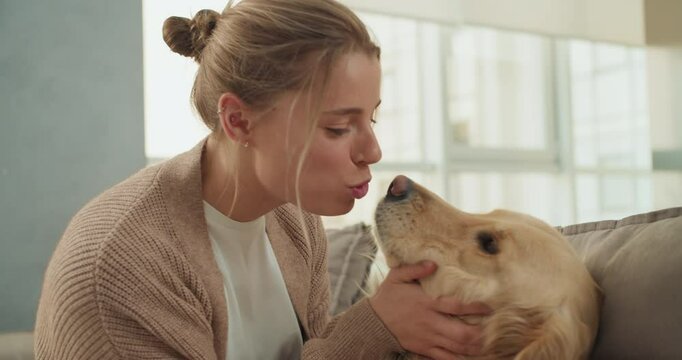 A young woman showing affection to her golden retriever on a cozy couch in a modern living room, expressing love and connection through a gentle touch and warm interaction