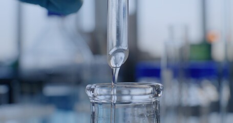 Advanced medical science lab: Close up of chemist pouring liquid through dropping funnel into glass flask. Professional scientist conducts chemical experiment using laboratory equipment. Chemistry.