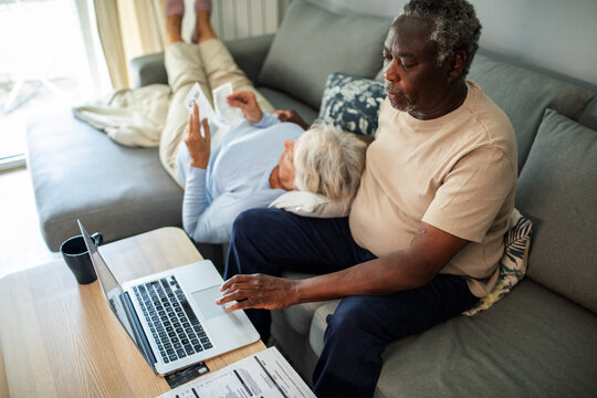 Diverse senior couple reading bills on the couch at home