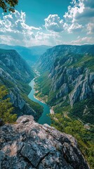 Breathtaking view of a river winding through majestic mountains under a bright blue sky with fluffy clouds.