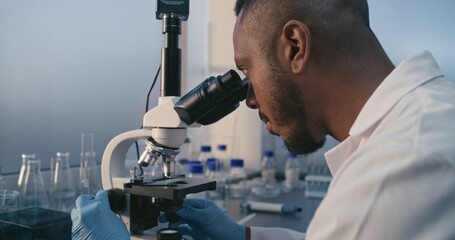African American male microbiologist or scientist uses high tech equipment to examine samples under modern microscope in medical laboratory. Drug development. Discoveries in pharmacology. Close up.