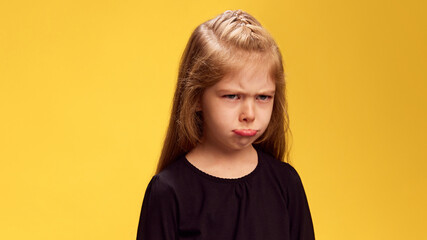 Girl's pouty face, complete with furrowed brows, perfectly conveys mood of frustration or sadness against yellow studio background. Concept of children's emotions, frustration, sadness. Ad