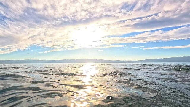 Sunset over Lake Ohrid during golden hour, with soft clouds in the sky and reflections of the setting sun on the clear water. Perfect for projects requiring serene nature scenes.