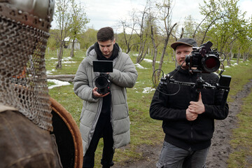 People operating professional camera equipment on location for historical reenactment. One person...