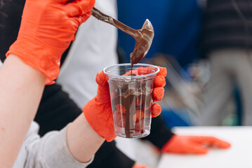cook pours hot chocolate into plastic cup with strawberries, cooking sweets outside