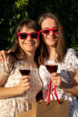 Portrait of a two young woman in sunglasses holding glasses with wine	