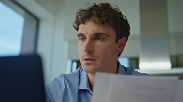 Serious man reviewing paperwork looking laptop at remote office closeup. 