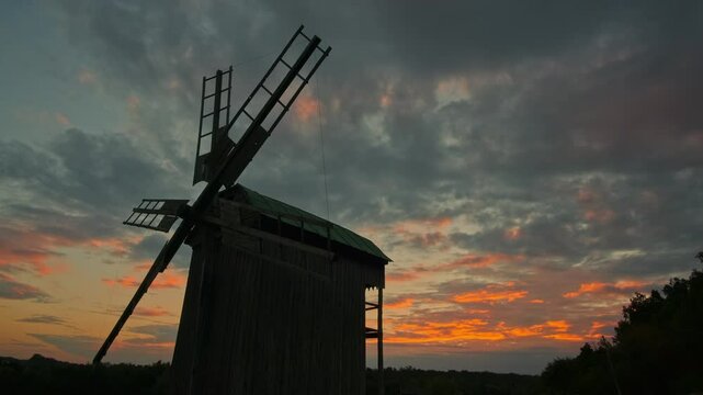 Old windmill at sunset with vibrant clouds in the sky.