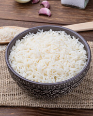 Cooked white rice in a bowl over wooden table with onion, bay leaf and garlic