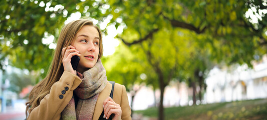 Young woman walking in a park with smartphone in her hands. Speaking on phone or sending messages outdoors