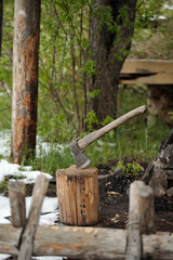Wooden-handled axe embedded in weathered tree stump surrounded by rustic wooden fence with patches of snow and trees