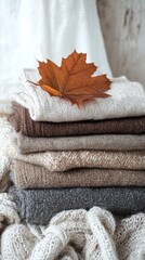 Cozy stacked sweaters with an autumn leaf, perfect for a warm fall atmosphere.