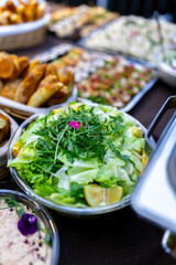 Fresh salad with greens and herbs served at a banquet alongside various dishes in a vibrant dining setting
