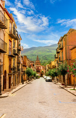 beautiful old european street with ancient church tower and nice vintage buildings and amazing green mountain hills and cloudy sky on background of wondetful travel landscape