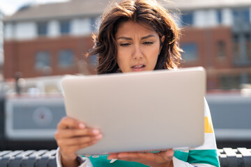 Woman focused on laptop outdoors in an urban setting with sunlight on a bright day