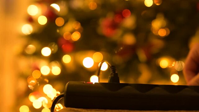 Turning off garland lights on Christmas tree. Man hand unplugging christmas lights from the outlet, end of celebration, cleaning up all decorations after winter holidays