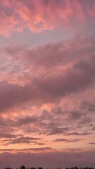 Naklejka premium A peaceful early morning sky at dawn with low-hanging, fluffy clouds in soft shades of pink and orange, the sun just starting to peek over the horizon 