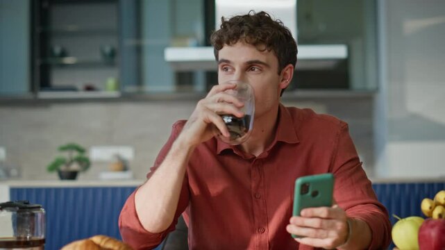 Cellphone man drinking coffee reading message at breakfast in kitchen closeup.