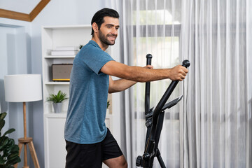 Athletic and sporty man running on elliptical running machine during home body workout exercise session for fit physique and healthy sport lifestyle at home. Gaiety home exercise workout training.