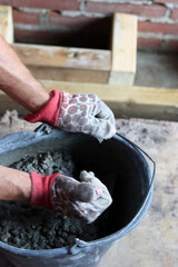 Hands in gloves holding a bucket with cement for building a house