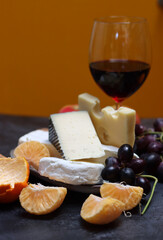 Glass of red wine with cheese, grapes and apples on grey background with copy pace. 
