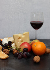 Cheese platter with grapes, red wine and apple on a gray background