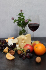 Still life with Dutch cheese and seasonal fruit on dark grey textured background with space for text. 