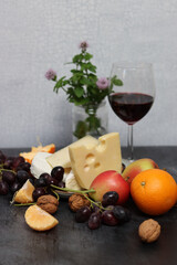 Cheese platter with grapes, red wine and apple on a gray background