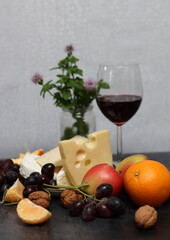 Still life with Dutch cheese and seasonal fruit on dark grey textured background with space for text. 