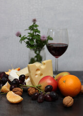 Cheese platter with grapes, red wine and apple on a gray background