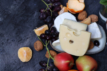 Still life with Dutch cheese and seasonal fruit on dark grey textured background with space for text. 